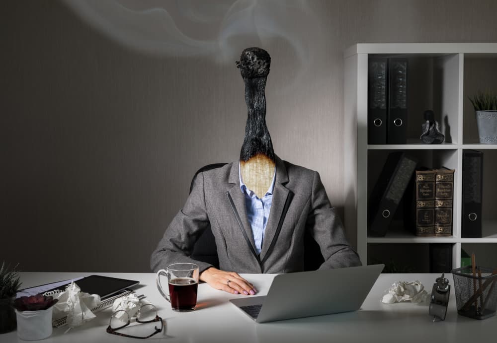 Person with burnt matchstick head at desk, symbolizing workplace burnout.